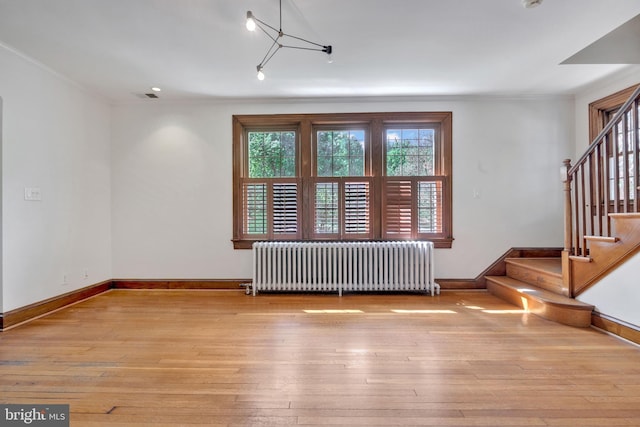 unfurnished living room with wood-type flooring, radiator heating unit, visible vents, and stairway