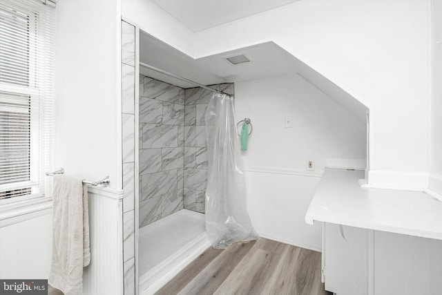 full bathroom with wood finished floors, a wainscoted wall, and a tile shower