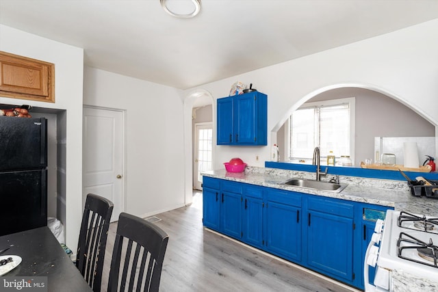 kitchen featuring a sink, white gas range, arched walkways, blue cabinets, and plenty of natural light
