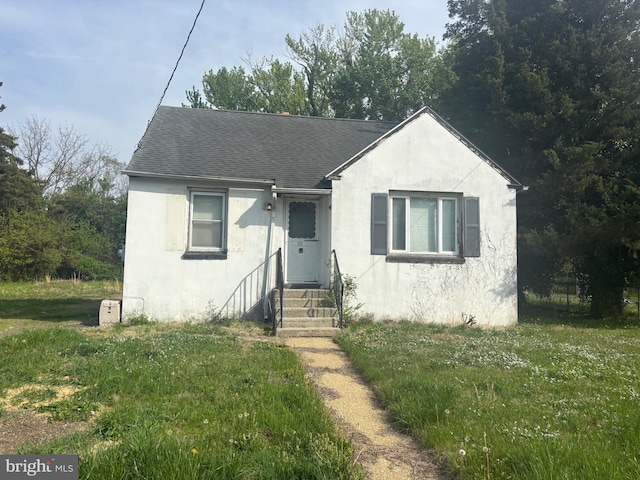 bungalow-style home with roof with shingles, a front yard, stucco siding, and fence