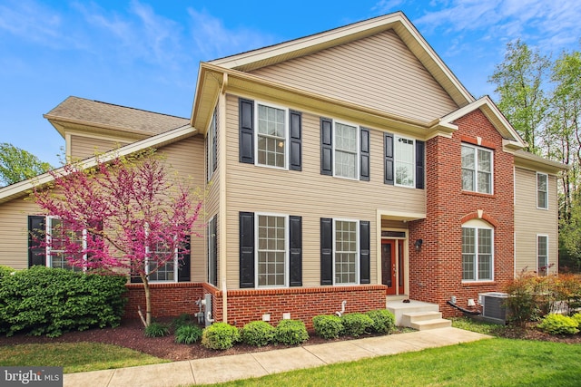 view of front facade featuring brick siding, central AC unit, and a front yard