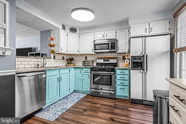 kitchen with dark wood-style flooring, a textured ceiling, white cabinets, a sink, and appliances with stainless steel finishes
