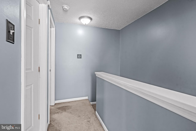 hall featuring carpet floors, baseboards, a textured ceiling, and an upstairs landing