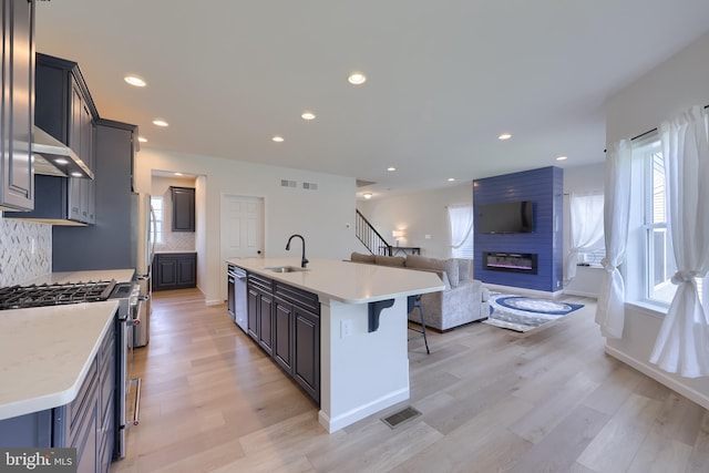 kitchen featuring appliances with stainless steel finishes, a sink, a fireplace, open floor plan, and visible vents