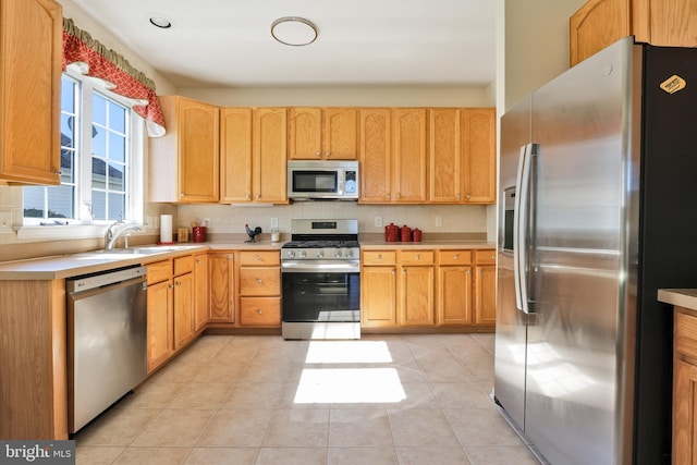 kitchen with a sink, decorative backsplash, light tile patterned floors, stainless steel appliances, and light countertops