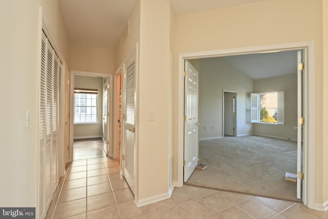hall featuring baseboards, light tile patterned floors, and light colored carpet