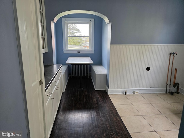 laundry room featuring radiator heating unit, baseboards, wood finished floors, and wainscoting