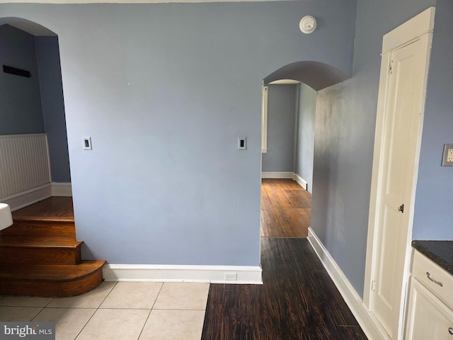 hallway with wood finished floors, baseboards, and arched walkways