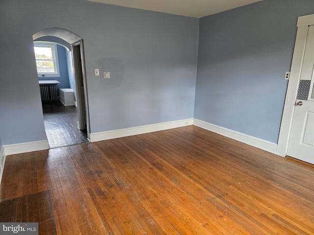 empty room with radiator, arched walkways, hardwood / wood-style floors, and baseboards