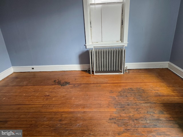 spare room with radiator, wood finished floors, and baseboards