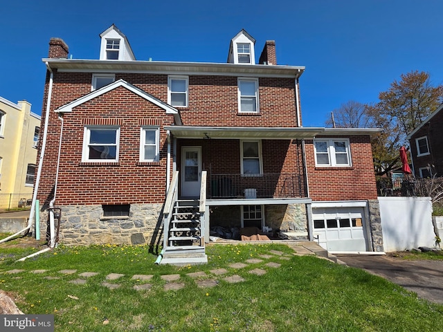 rear view of property with a chimney, brick siding, aphalt driveway, and a garage