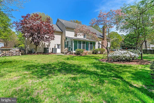rear view of property featuring a lawn, central AC unit, and a sunroom