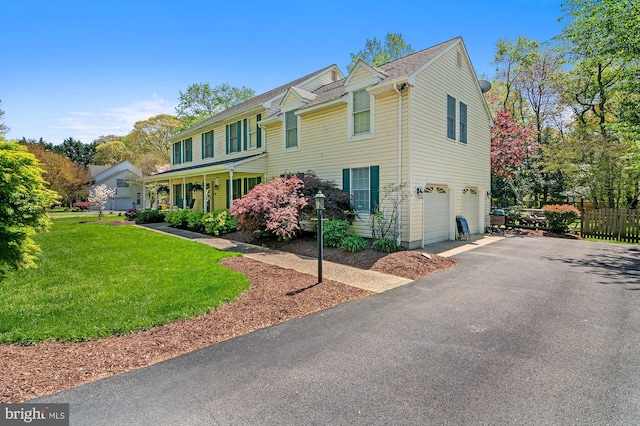 colonial inspired home with an attached garage, aphalt driveway, fence, and a front yard