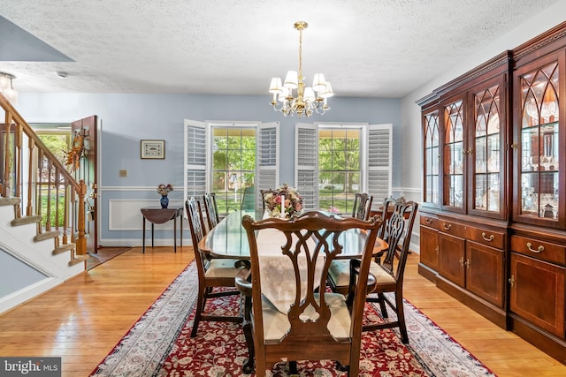 dining area featuring an inviting chandelier, a textured ceiling, light wood finished floors, and stairway