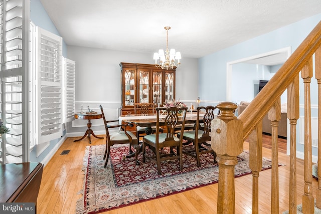 dining area featuring wood-type flooring, visible vents, stairway, and an inviting chandelier