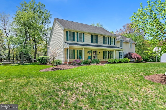 colonial house featuring covered porch, fence, and a front yard