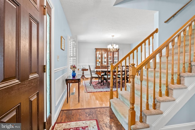 foyer entrance featuring a notable chandelier, a textured ceiling, a wainscoted wall, wood finished floors, and stairway