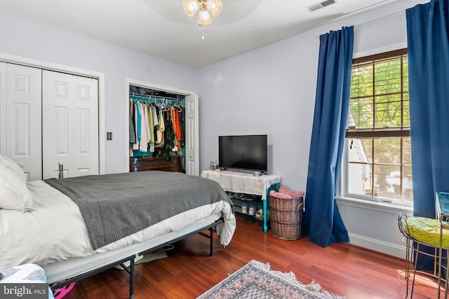 bedroom featuring visible vents, wood finished floors, multiple windows, and two closets