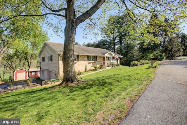 view of front facade featuring driveway, a storage shed, a front lawn, brick siding, and a garage