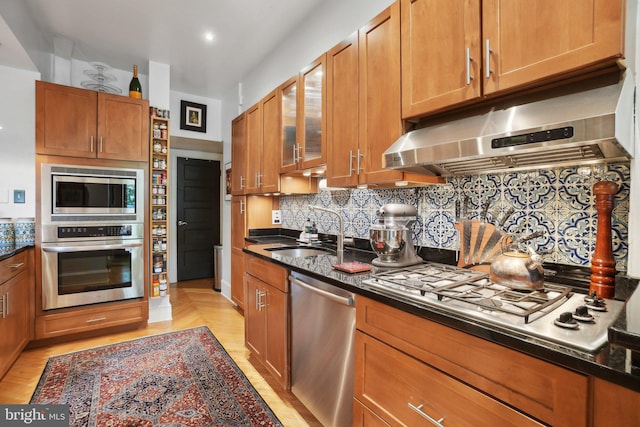 kitchen featuring decorative backsplash, glass insert cabinets, under cabinet range hood, a sink, and appliances with stainless steel finishes