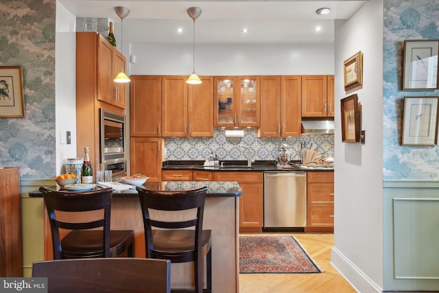 kitchen with a kitchen bar, dark countertops, stainless steel dishwasher, a sink, and wallpapered walls