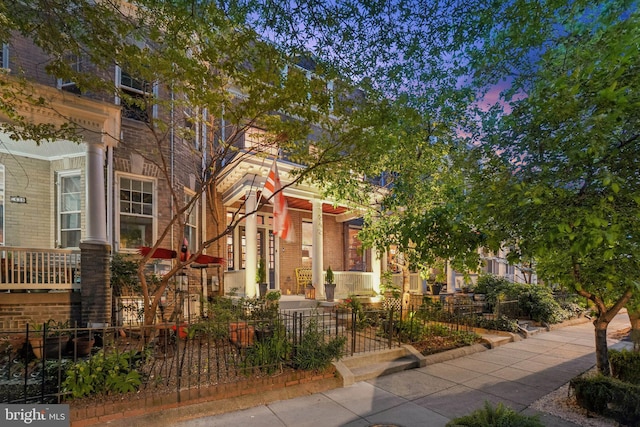view of front facade featuring covered porch, a fenced front yard, and brick siding