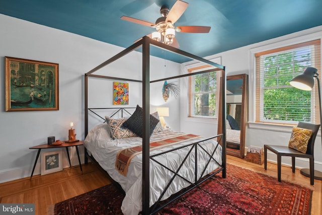 bedroom with baseboards, a ceiling fan, wood finished floors, and multiple windows