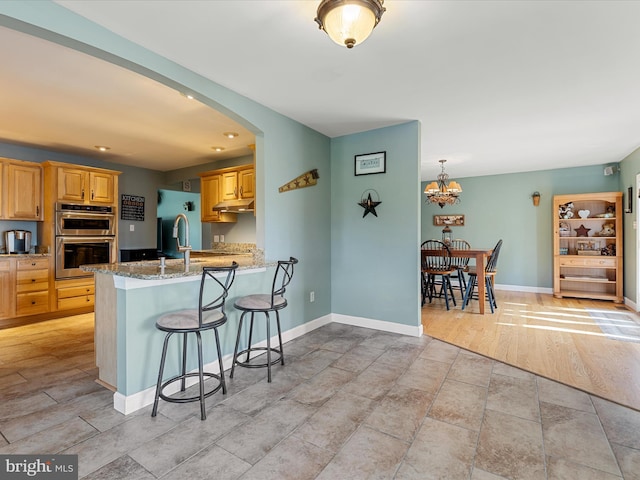 2004 State Road 259 N, Wardensville, WV 26851 - kitchen featuring light stone countertops, a kitchen breakfast bar, stainless steel double oven, under cabinet range hood, and a sink