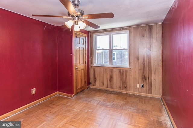 empty room with baseboards, ceiling fan, and wooden walls