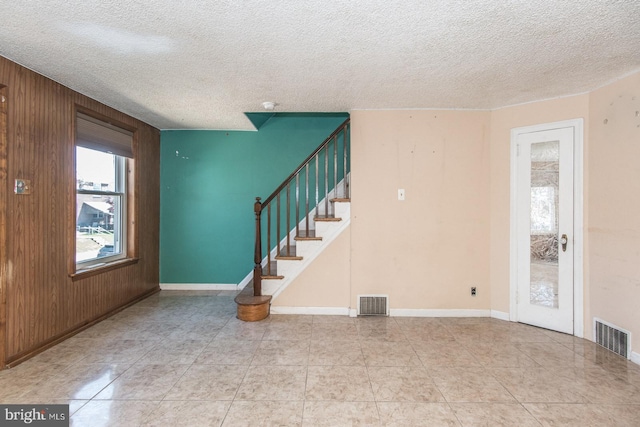 unfurnished living room featuring wooden walls, a textured ceiling, visible vents, and stairway