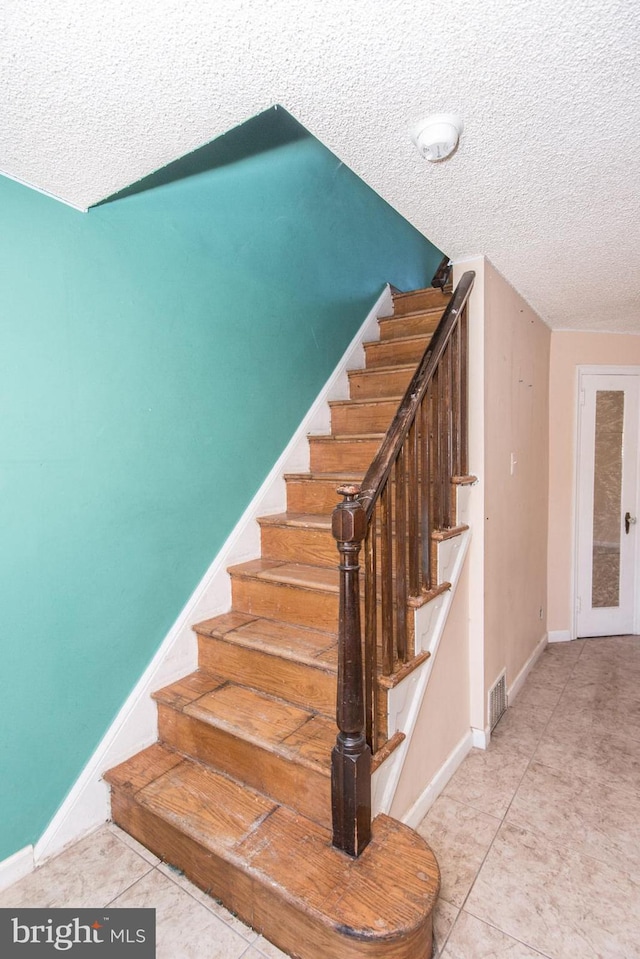 stairs featuring a textured ceiling, visible vents, baseboards, and tile patterned flooring