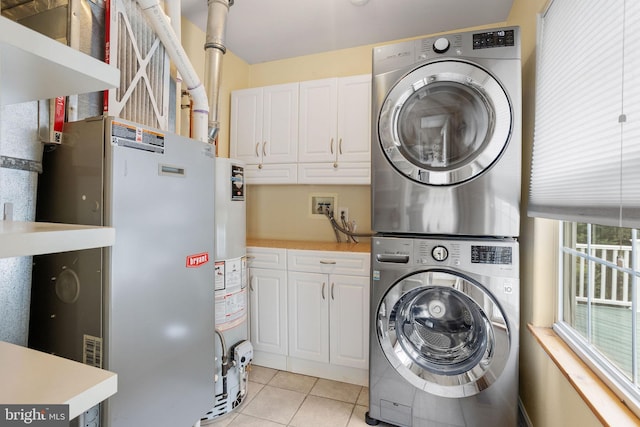 washroom featuring stacked washing maching and dryer, light tile patterned floors, water heater, and cabinet space