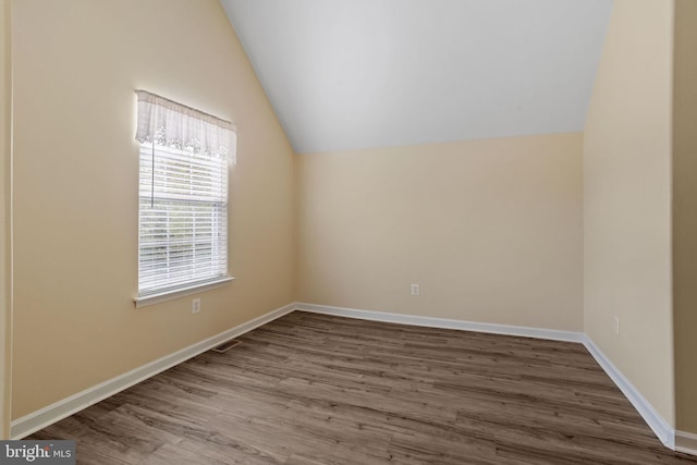 spare room with baseboards, wood finished floors, and vaulted ceiling