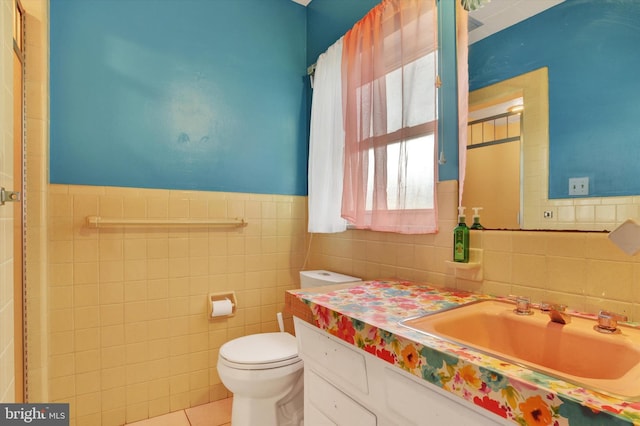 bathroom with tile walls, vanity, tile patterned floors, toilet, and wainscoting