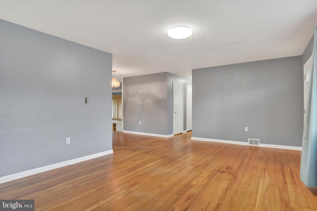 empty room with baseboards, visible vents, an inviting chandelier, and light wood-style flooring