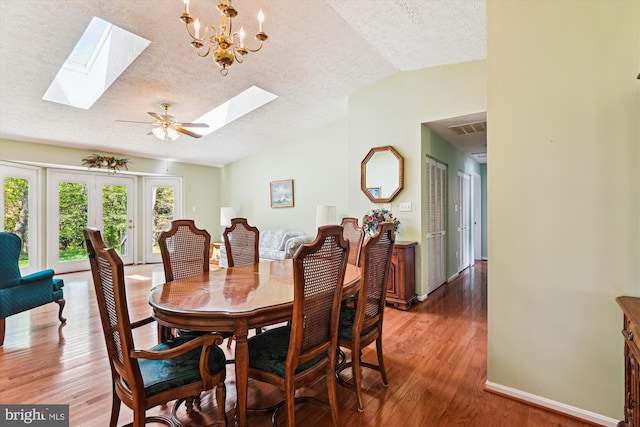 dining area featuring lofted ceiling with skylight, visible vents, baseboards, a textured ceiling, and wood finished floors