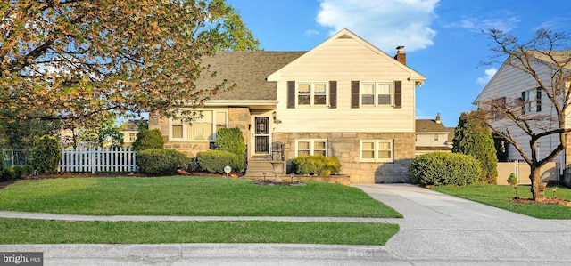 tri-level home featuring a chimney, a front lawn, fence, and stone siding