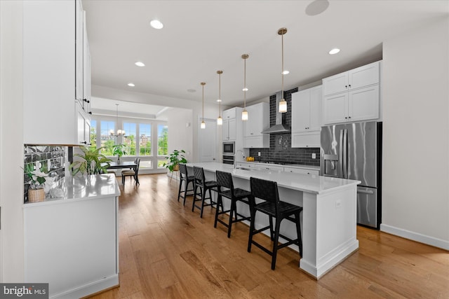 kitchen with stainless steel appliances, wall chimney exhaust hood, light countertops, a breakfast bar area, and light wood-style floors