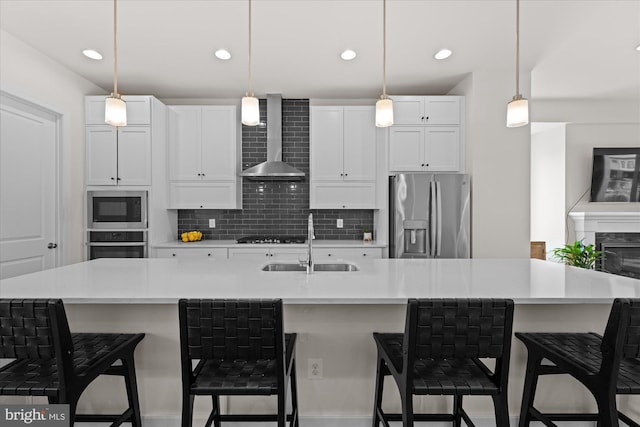 kitchen with stainless steel appliances, wall chimney range hood, a sink, decorative backsplash, and white cabinetry