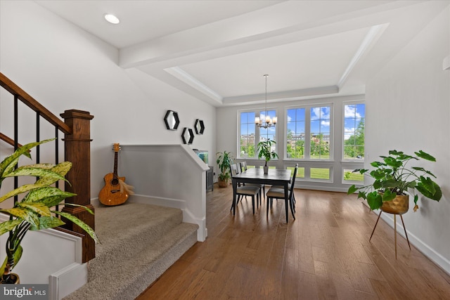 stairway featuring baseboards, a chandelier, wood finished floors, and a raised ceiling