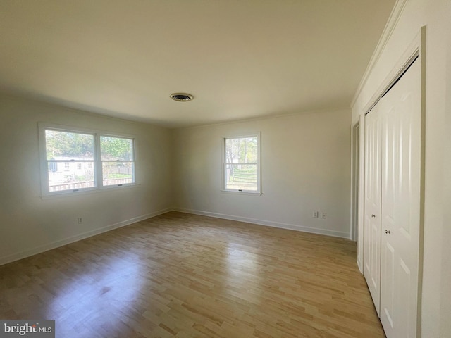 unfurnished bedroom featuring baseboards, multiple windows, light wood finished floors, and a closet