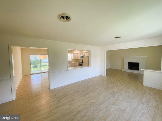 unfurnished living room with a fireplace, ornamental molding, visible vents, and light wood-style flooring