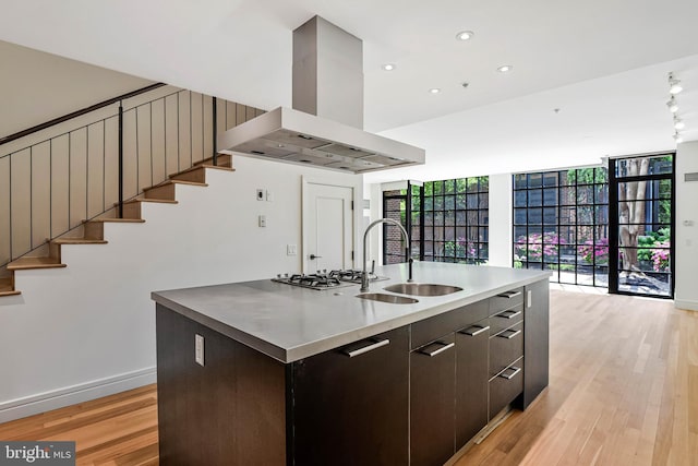 kitchen with dark brown cabinetry, a sink, light wood-style floors, a kitchen island with sink, and range hood