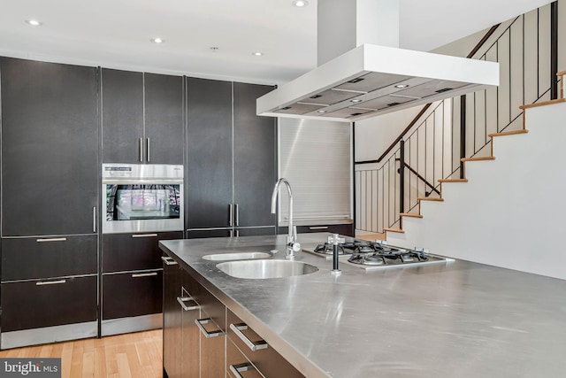 kitchen with appliances with stainless steel finishes, ventilation hood, stainless steel countertops, recessed lighting, and light wood-type flooring
