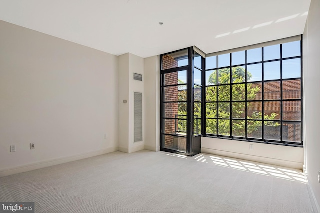 carpeted spare room with baseboards, visible vents, and expansive windows