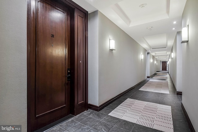 hallway with baseboards, dark tile patterned floors, and a tray ceiling