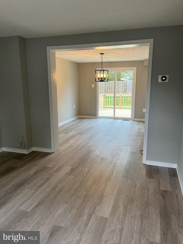 spare room featuring baseboards, a chandelier, and wood finished floors