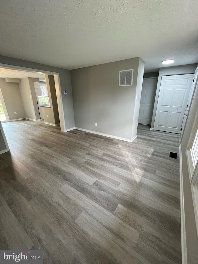 interior space featuring visible vents, a textured ceiling, baseboards, and dark wood-type flooring