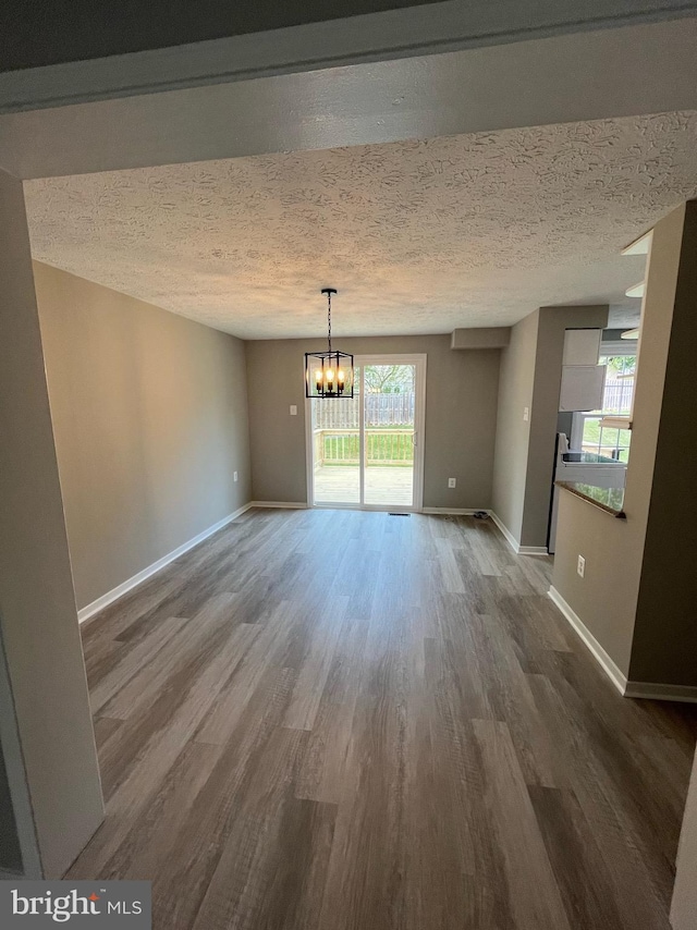 unfurnished dining area with an inviting chandelier, a textured ceiling, baseboards, and dark wood-type flooring