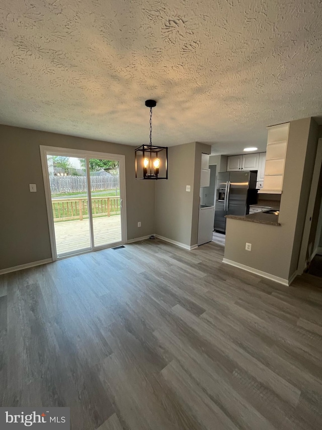 unfurnished dining area featuring a textured ceiling, a chandelier, baseboards, and dark wood-type flooring